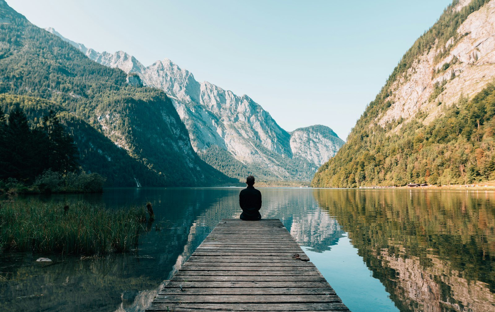 Une personne assise au bout d’un ponton, face à un lac de montagne immobile