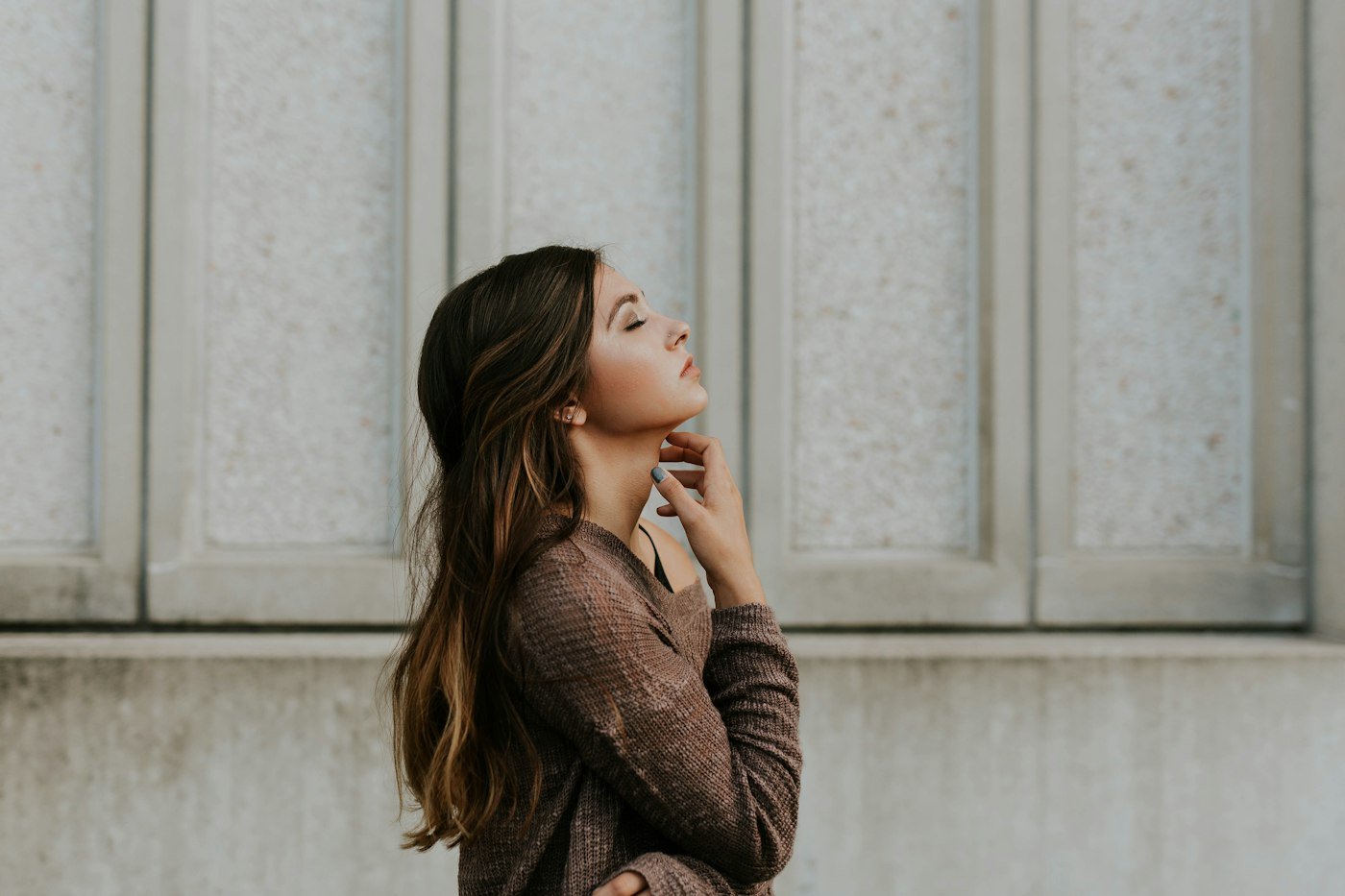 Une femme, les yeux levés, la main posée sur le cou, dans un moment de respiration et de présence à soi